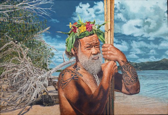 Homme tatoué avec une couronne de fleurs, tenant un bâton sur une plage ensoleillée.