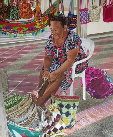 Femme assise, tissant des sacs colorés, entourée de créations textiles.