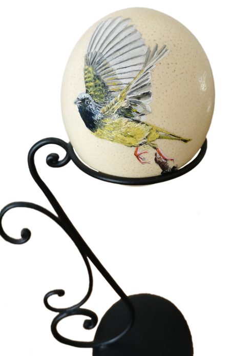 Un œuf décoré avec un oiseau coloré posé sur un support en métal.