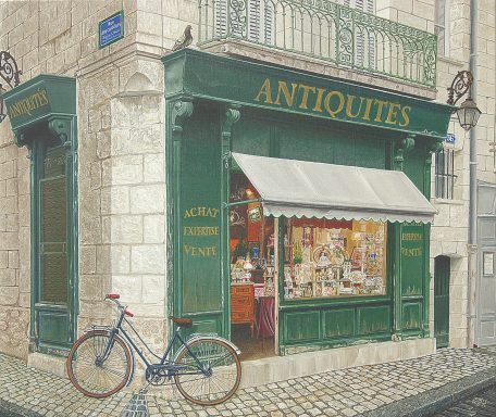 Boutique d'antiquités avec vitrine éclairée, vélo garé devant, dans une rue pavée.